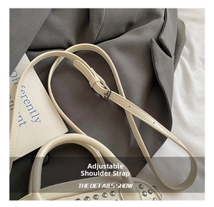 Detail of adjustable thin strap and silver rivets on a cream faux leather crossbody bag
