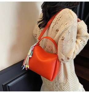 Détail d'un sac seau orange vif en cuir grainé avec un gland de franges coloré