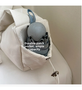 Close-up of beige dumpling bag side pocket with adjustable drawstring holding a folded umbrella