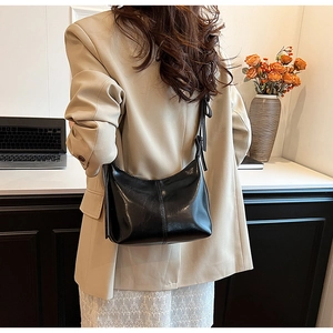 Close-up of a stylish black glossy hobo bag with adjustable strap in a cozy office setting
