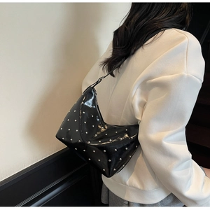 Close-up of black patent leather shoulder bag with silver studs and crescent silhouette