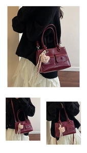 Detail view of burgundy tote bag with side pockets and plush bear charm decoration