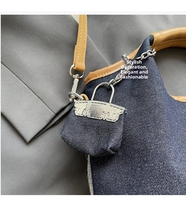 Detail of a mini dark blue denim bag charm with silver hardware on a leather tote