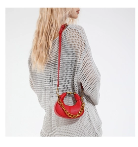 Detail view of red lychee textured crescent bag with gold chain strap on a white sweater