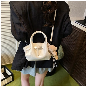 Detail view of a white crocodile embossed handbag with a cute brown plush bear charm