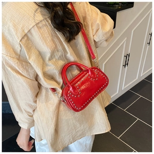 Crossbody view of a red glossy handbag featuring silver rivets and a slim leather strap
