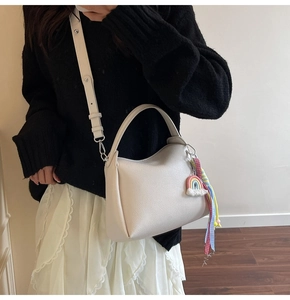 Détail du sac seau en cuir grainé crème avec breloque arc-en-ciel à pompons colorés