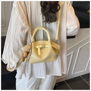 Detail view of light yellow crocodile texture handbag with cute bear charm and strap