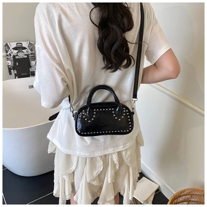 Detail of a black studded mini crossbody bag worn by a model in a minimalist room