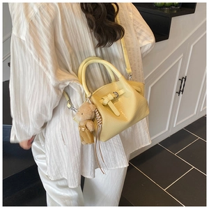 Detail view of yellow faux-crocodile bucket bag with cute brown bear charm on shoulder