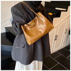 Detail of camel quilted tote bag with gold chain strap and metal turn-lock on model