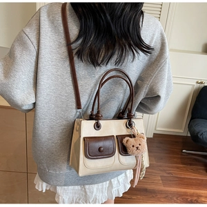 Detailed back view of a beige color-block crossbody bag with two pockets and a plush bear toy