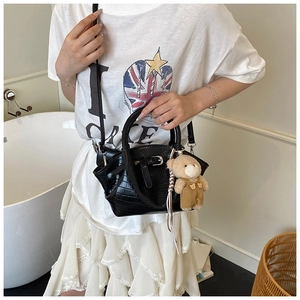Detail of black faux crocodile leather handbag with plush bear charm and sturdy top handle