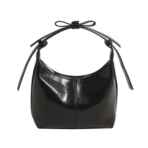 Detail of a black glossy leather crescent bag featuring a stylish bow on the handle strap