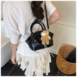 Detail view of black faux-crocodile texture bucket bag with a cute plush bear charm