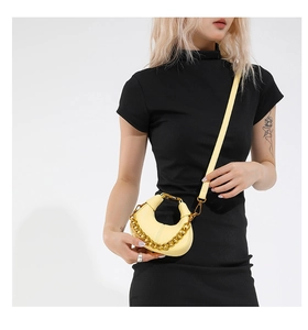 Détail du sac croissant jaune avec chaîne dorée porté par un mannequin en robe noire