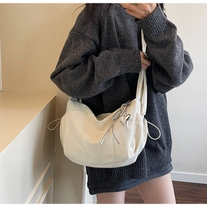 Detail of white half-moon crossbody bag with silver heart pendant and drawstring feature