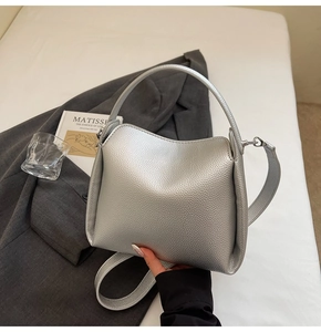Vue détaillée du sac seau argenté en cuir grainé sur un lit blanc minimaliste