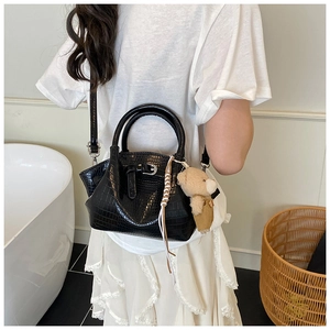 Detail of black crocodile texture handbag with plush bear charm and woven strap