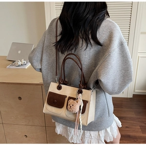 Detailed view of beige crossbody bag with brown pockets and a plush bear charm