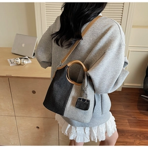 Detail of dual-tone denim bucket bag with brown leather handles and mini charm