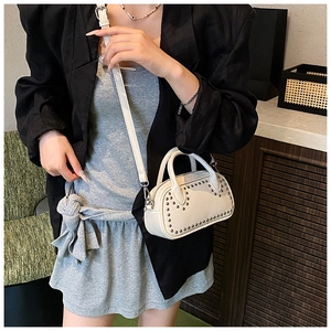Close-up of white leather handbag featuring stylish silver rivets and a secure zipper closure