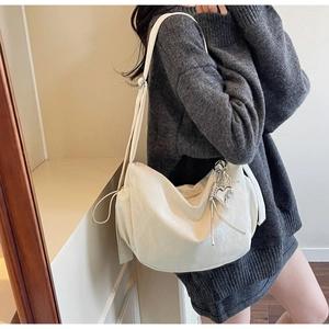 Detail of a creamy white hobo bag featuring a silver heart charm and adjustable strap