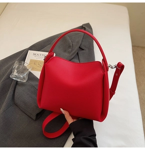 Détail du sac seau rouge avec texture grainée et garnitures argentées sur lin blanc