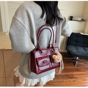 Macro view of dark red leather handbag featuring dual front buckle pockets and charm