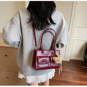 Detail of dark red retro PU leather handbag with decorative pockets and a plush bear charm
