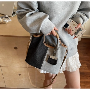 Detail of color-block denim bucket bag featuring brown leather handles and silver chain lock