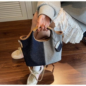 Detail of two-tone denim bucket bag with brown leather handles and mini pouch accessory