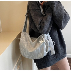 Detail of silver textured dumpling bag with metal heart pendant and wide shoulder strap