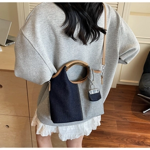 Rear view of a model wearing a two-tone denim bucket bag with brown leather handles