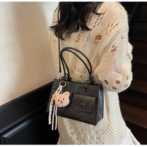 Detail of black rectangular PU leather handbag with plush bear charm and ribbon decor