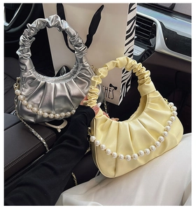 Detail of pleated cloud handbags with pearl handles in silver and yellow displayed in a car