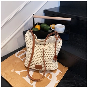 Detail of woven straw tote bag featuring white crochet pattern and brown leather straps
