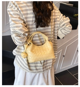 Détail du sac seau tissé beige montrant l'anse nouée et la bandoulière chaîne dorée