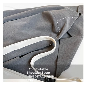 Detail of grey studded tote bag with wide white leather strap and visible stitching