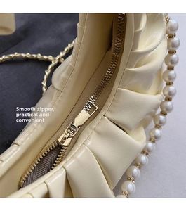 Detail of a creamy cloud bag showing smooth metal zipper and elegant pleated texture