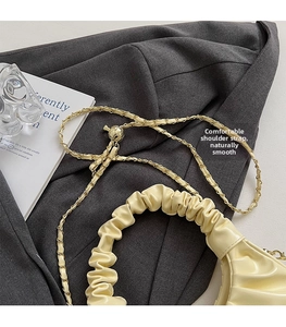 Detail of cream pleated cloud bag featuring soft handles and golden chain shoulder strap