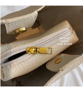 Detail of beige bucket bag featuring smooth metal zipper and magnetic gold closure