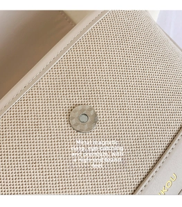 Detailed macro view of metal magnetic buckle and cream fabric on a crossbody bag