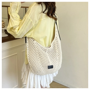 Detail of white crochet knit tote bag with crescent shape and minimalist black leather tag