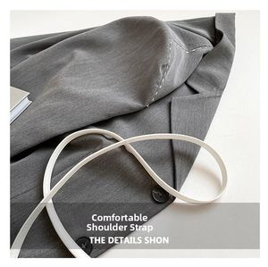 Détail d'une bandoulière blanche et d'un bouton noir sur un tissu texturé gris chic