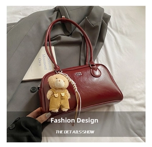 Détail d'un sac à main en cuir verni bordeaux avec charm ours sur fond de blazer gris