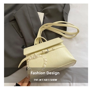 Detail of cream women's shoulder bag with heart lace pendant and textured faux leather