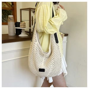Close-up of a cream crochet tote bag with black leather straps and square logo patch