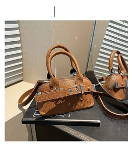 Détail d'un sac à main marron à motif litchi avec boucle argentée posé sur un livre noir