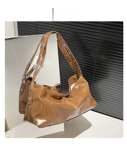 Détail d'un sac hobo en cuir marron avec bandoulière large ornée d'œillets argentés